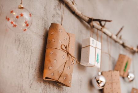 Christmas gifts Packed with Kraft paper and hand made decorations hang on a rope tied to a stick against a gray concrete wall. Concept of holiday and new year 2020 at homeの写真素材