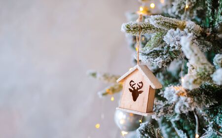 Decorated snow-covered Christmas tree close-up. Wooden toy house illuminated garland. Christmas baubles Macro photo with bokeh. concept winter holiday light decorations. new year 2020 free space textの写真素材