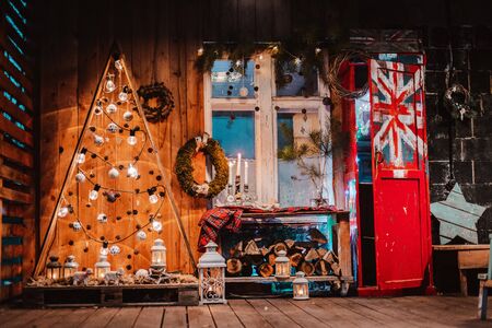 Winter wooden exterior night veranda country house with Christmas decorations rustic vintage style with painted British flag. Creative decoration of Christmas tree natural brooms with lights garlands.の写真素材