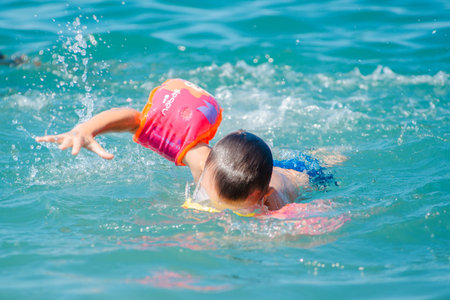 small child swims in armbands in the sea. Childrens swimming training.のeditorial素材