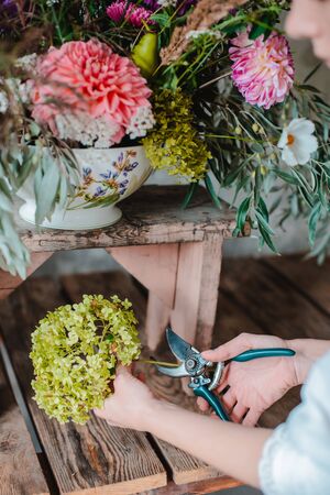 Female professional florist prepares the arrangement of wild flowers. Flower shop. Background concrete gray wall. Concept inspiration, floral, greetings, spring, ornament flowers.の写真素材