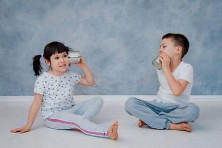 A young brother and sister are talking to a tin phone against a gray wall. The concept of childrens communication.の写真素材