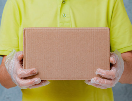 The courier holds cardboard boxes in disposable gloves. Contactless delivery during the quarantine...