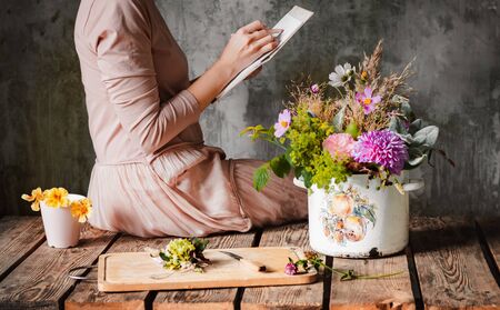 female artist draws a composition of wild flowers in a pot in a rustic style, a sketchbook on a table with pencils. Sketch art, artist inspiration, design, hobby, drawing school. hands close upの写真素材