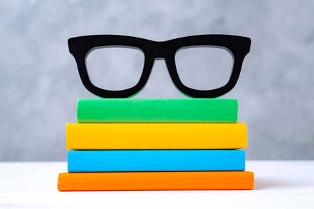 stack of colorful books with glasses on a white wooden table against a gray wall. The concept of going back to school, reading, library, literature, study, education.の写真素材