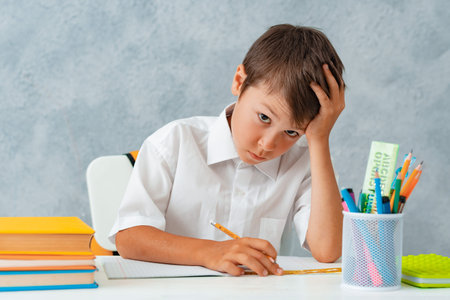 back to school. Happy smiling student draws at the Desk. A schoolboy solves his homework. A boy from...