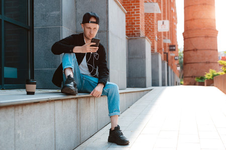 trendy stylish guy in a black cap and sunglasses with a smartphone and headphones on the background...
