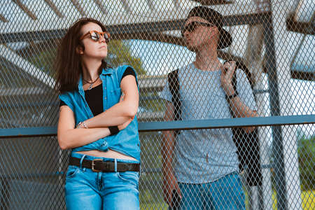 young stylish pair hipsters sunglasses, guy girl urban space separated cage fence. concept relationship between man woman, disagreements, misunderstandings conflict, depression, different sidesの写真素材