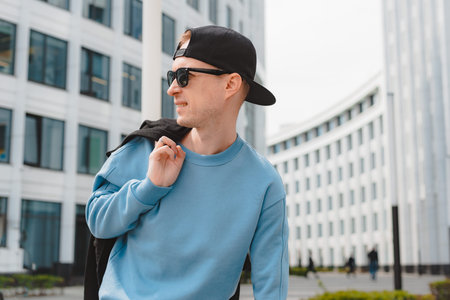 Young free beautiful fashionable hipster guy walking down the street, wearing a cap sunglasses,...