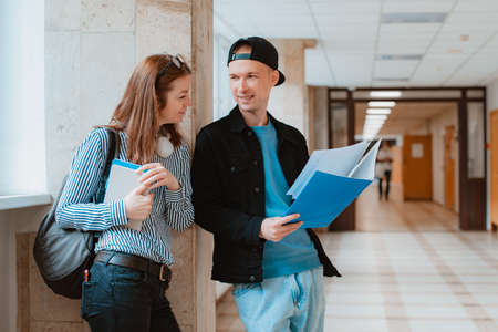 Two students, a guy and a girl, are walking along the corridor of the university and discussing educational material.の写真素材