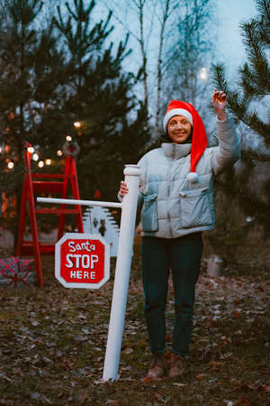 hipster woman wearing a Santa Claus hat at night with a sparkler lights up a stop sign with the text Santa stop here.の写真素材