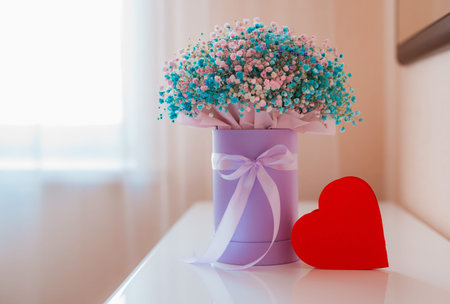 paper heart symbol, a gift box with a bouquet of colored gypsophiles on the table in the room. The...