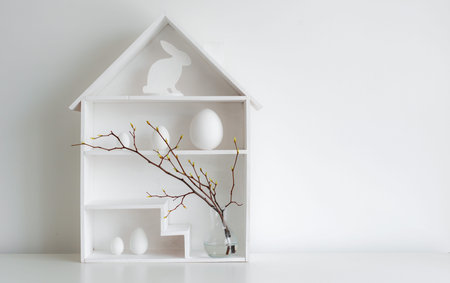 Home minimalist interior with Easter decor. Branches with budding buds in a glass vase on shelves in...