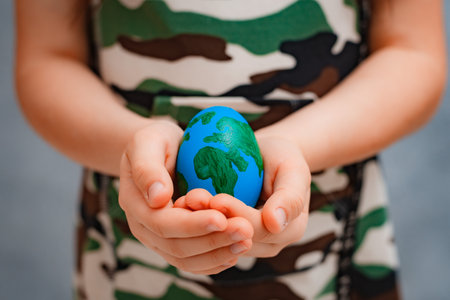 planet Earth in the shape of an egg in children's hands close-up. The concept of global problems of humanity, peace to the world, no war, military, soldier guardの写真素材