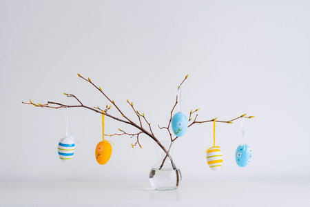 Minimalistic Easter still life. A glass vase with a branch on which colorful Easter eggs hang on a...