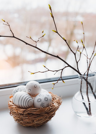 Easter composition. Willow branches in a vase, painted eggs in a nest on the windowsill by a wet window at sunset. spring timeの写真素材