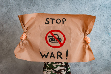 child raises a banner with the inscription no war, standing on the gray concrete background of the studio. No war, stop the war, peaceの写真素材