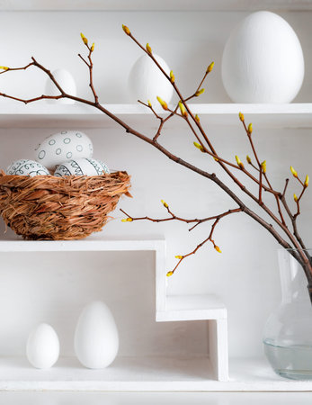 Home minimalist interior with Easter decor. Branches with budding buds in a glass vase on shelves in...