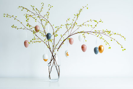 vase with spring branches of blossoming trees, colorful Easter eggs on a white tableの写真素材