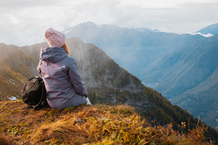 female tourist with a backpack enjoys the sunset at the top mountain