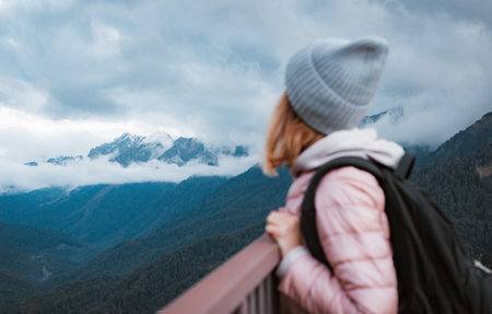 young woman smiling with a backpack in a hat, admiring looks at the mountains.