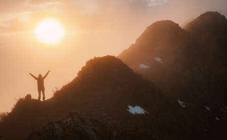 female tourist with a backpack in autumn on the mountain with outstretched arms welcomes admires the sunsetの写真素材