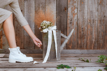 women's feet in dress and white shoes, fashion background wooden planks gardener iron watering can,...