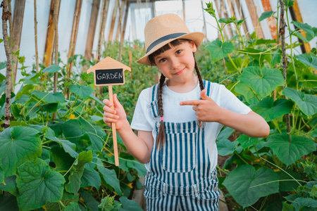 child girl straw hat greenhouse garden cucumbers summer chalk plaque board with inscription garden, seasonal gardening work. Little farmer helper. green living, eco friendly home grown, clean beautyの写真素材