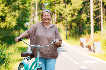 Senior older elderly modern woman rides a bicycle in a city park in the forest. Active pensioner, health lifestyleの写真素材