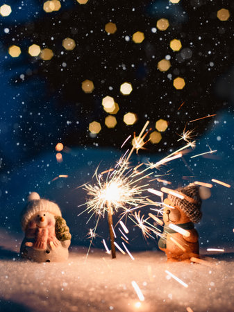 Merry Christmas. New Year's card Sparkler in the snow in the evening. two decorative figures a snowman and a bear in the snow outdoorsの写真素材
