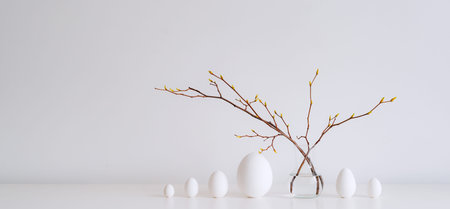 Minimalistic Easter still life. A glass vase with a branch on which colorful Easter eggs hang on a...