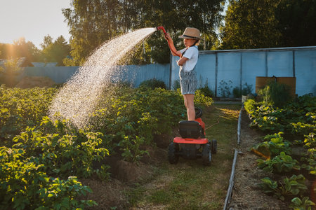Child watering plants garden. Kid with water hose sunny backyard. little girl gardening. Summer...