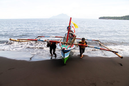 Two fishermen with wooden boat on the beachのeditorial素材