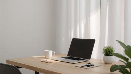 Modern workspace with laptop, coffee cup and other items on wooden table.の素材
