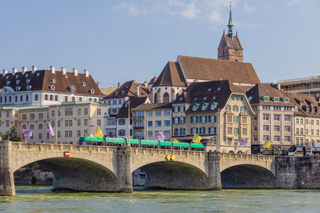 Basel city- A bridge spans Rhein river with a city in the background. The bridge is a stone...