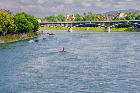 Basel city- A bridge spans Rhein river with a city in the background. The bridge is a stone...