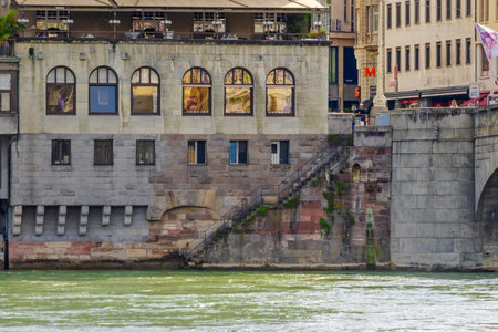 Basel city- A bridge spans Rhein river with a city in the background. The bridge is a stone...