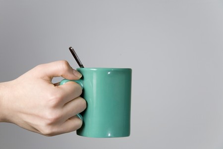 woman hand holding a tea cup with a spoon close-up, from left to centre, isolated on grayの写真素材