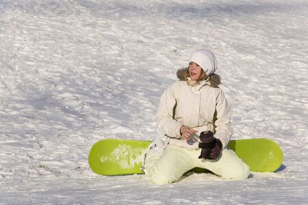 young woman sitting on snow with snowboardの写真素材