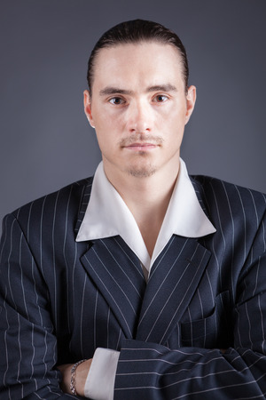 Young male confident male posing in gangster style suite. Studio isolated on gray background.の写真素材