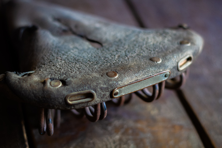 old style worn dry bicycle saddle on wooden surfaceの写真素材
