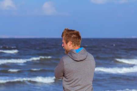 Thoughtful young man looking away at beach near open water at sunny day