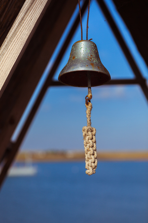 Old vintage rusty metal ship bell with a white rope on a blue sea backgroundの写真素材
