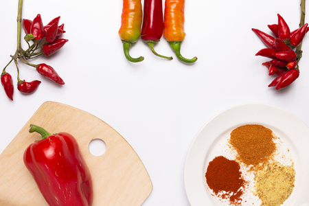 Assorted colorful varieties of hot and sweet peppers on white background with cutting board and plate with spicesの写真素材