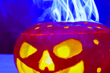 red Halloween pumpkin monster with yellow light coming from inside out of eyes, mouth and round holes emitting white blue smoke and neon light. closeup.の写真素材