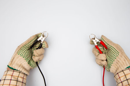 hands of electrician in protective gloves holding electric red and black clamps on white background