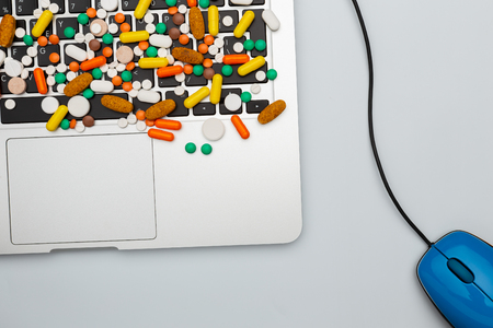 medicine drug pills and capsules of different type and color on computer keyboard and mouse closeup, on white background, top view, copy space. doctor work place, or sick of internet or social networkの写真素材