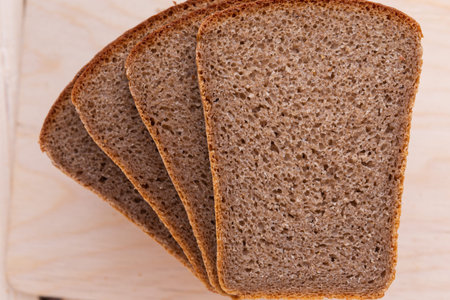 Slices of brick brown rye bread on wooden background desk, top view, closeup