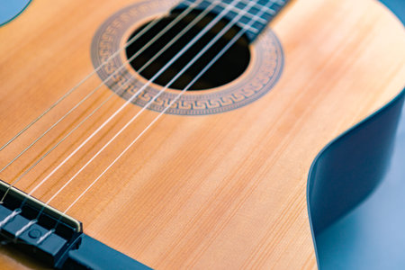 curved shape part of acoustic guitar yellow glossy wooden deck on blue background, fragment, shallow...
