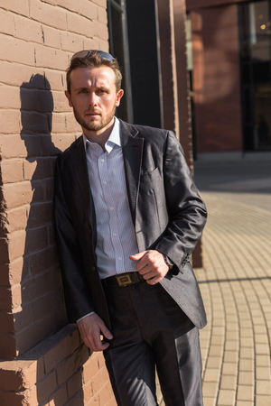 Half length portrait of young confident man in suit and sunglasses standing outside of his office building, prosperous male leader after business meetingの写真素材